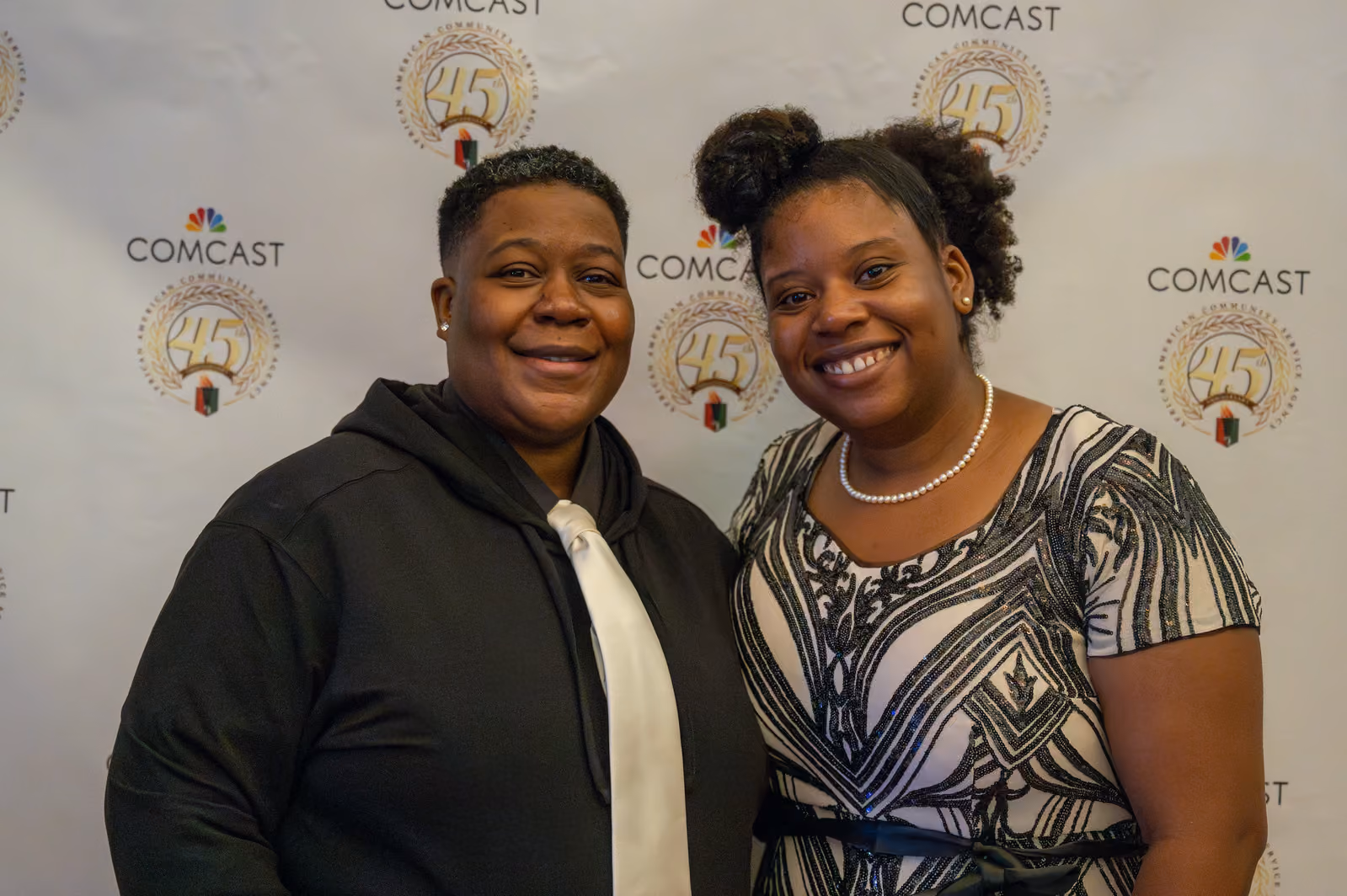 Two smiling guests pose before a backdrop with Comcast logos and 45th anniversary emblems