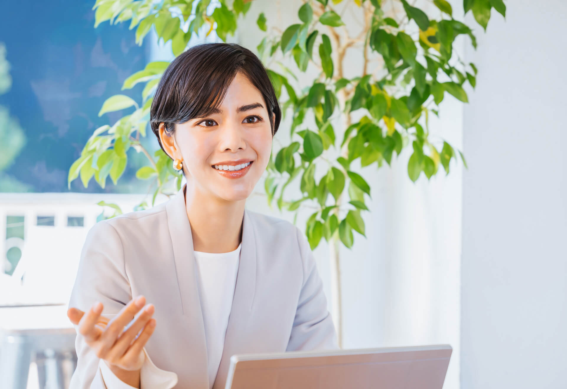 A smiling professional woman with short hair working in an office with indoor plants.