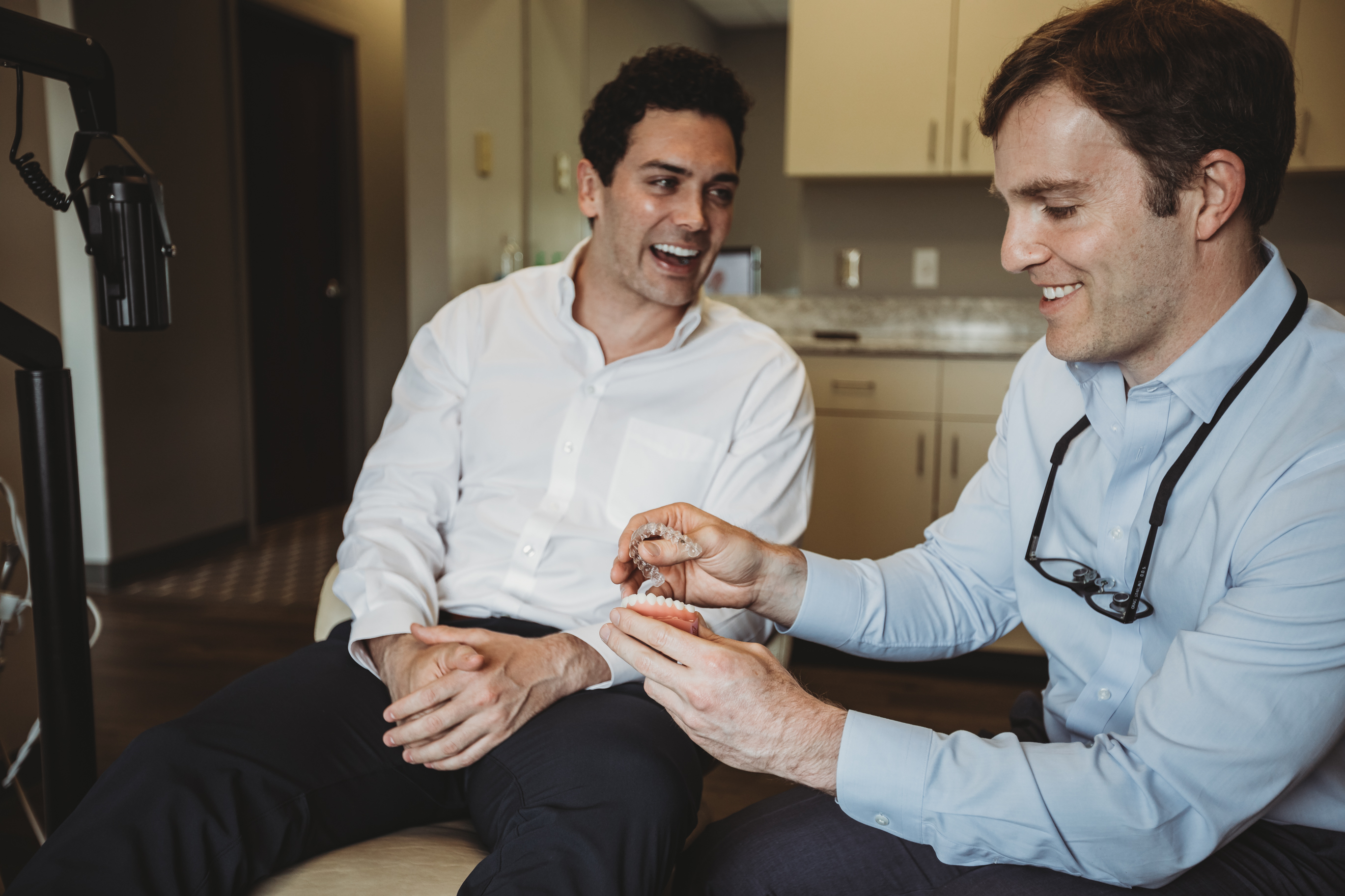 A smiling adult professional sits in dental office with orthodontist, exuding confidence with straight teeth, likely a result of adult orthodontic treatment. The image reflects the importance of oral health and self-confidence, showcasing the effectiveness of braces for adults in achieving a beautiful smile.