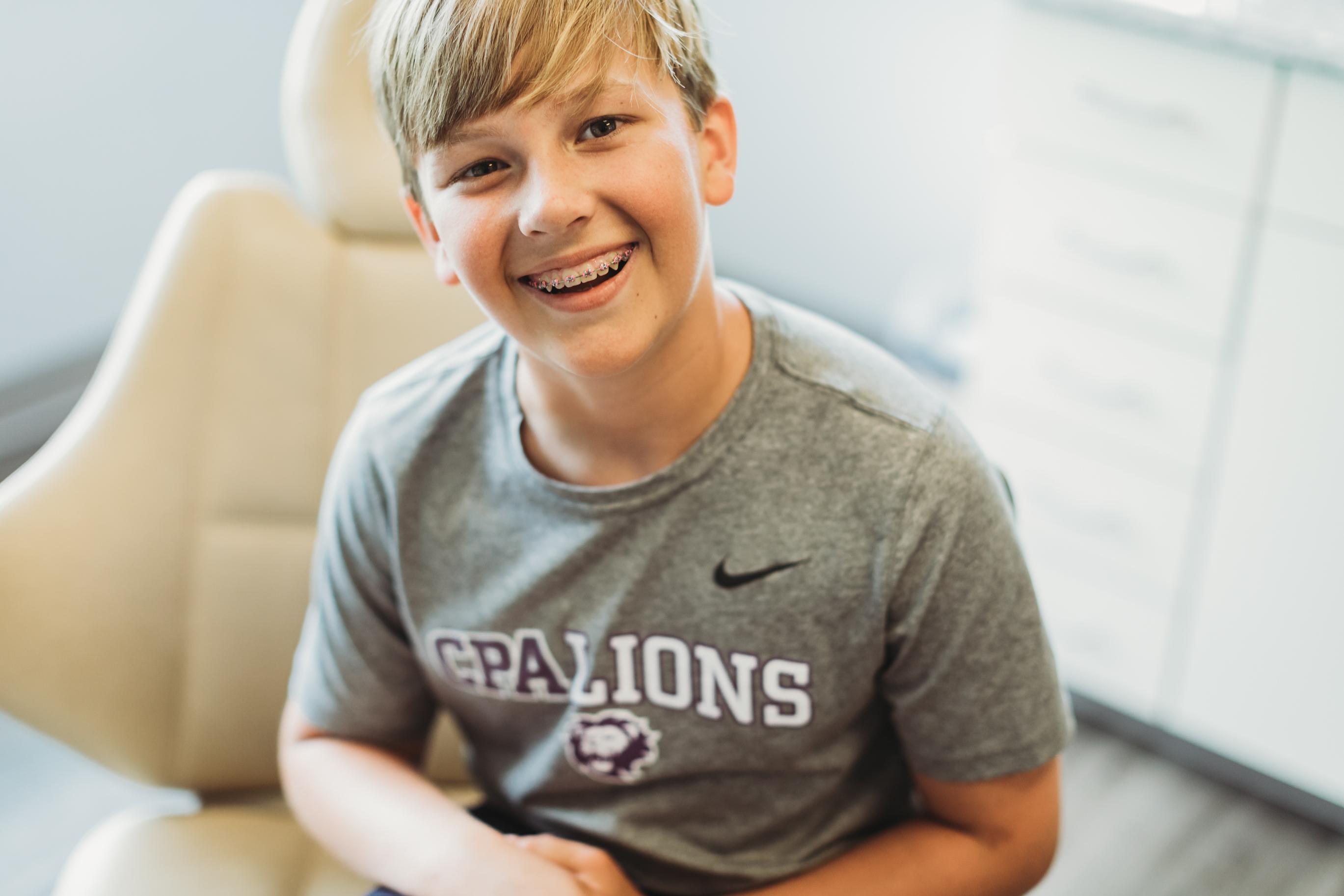 A cheerful teenager with traditional metal braces is smiling confidently, showcasing their orthodontic treatment journey. This image highlights the importance of early orthodontic evaluation for maintaining a child's oral health and ensuring proper dental development.