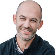 Smiling man with a beard and bald head wearing a dark shirt against a muted blue background.