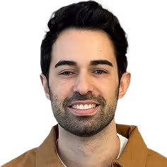 Smiling man with dark hair, beard, and mustache against a muted green background.