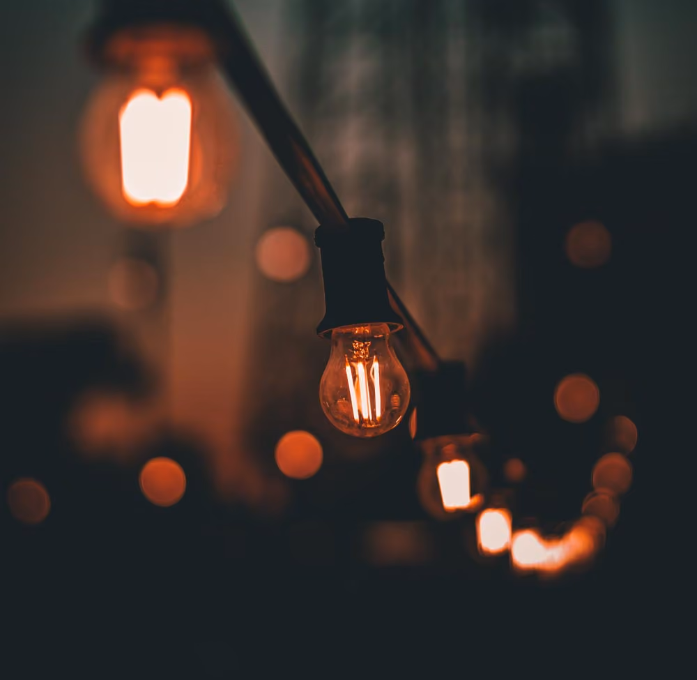 Close-up of glowing string light bulbs hanging in a dark setting, creating warm orange bokeh.