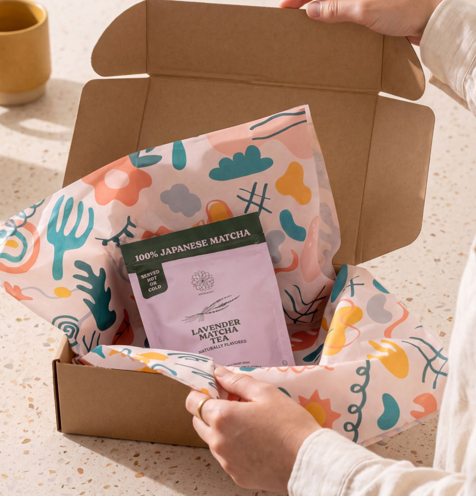 Hands opening a box with colorful wrapping paper holding lavender matcha tea package.
