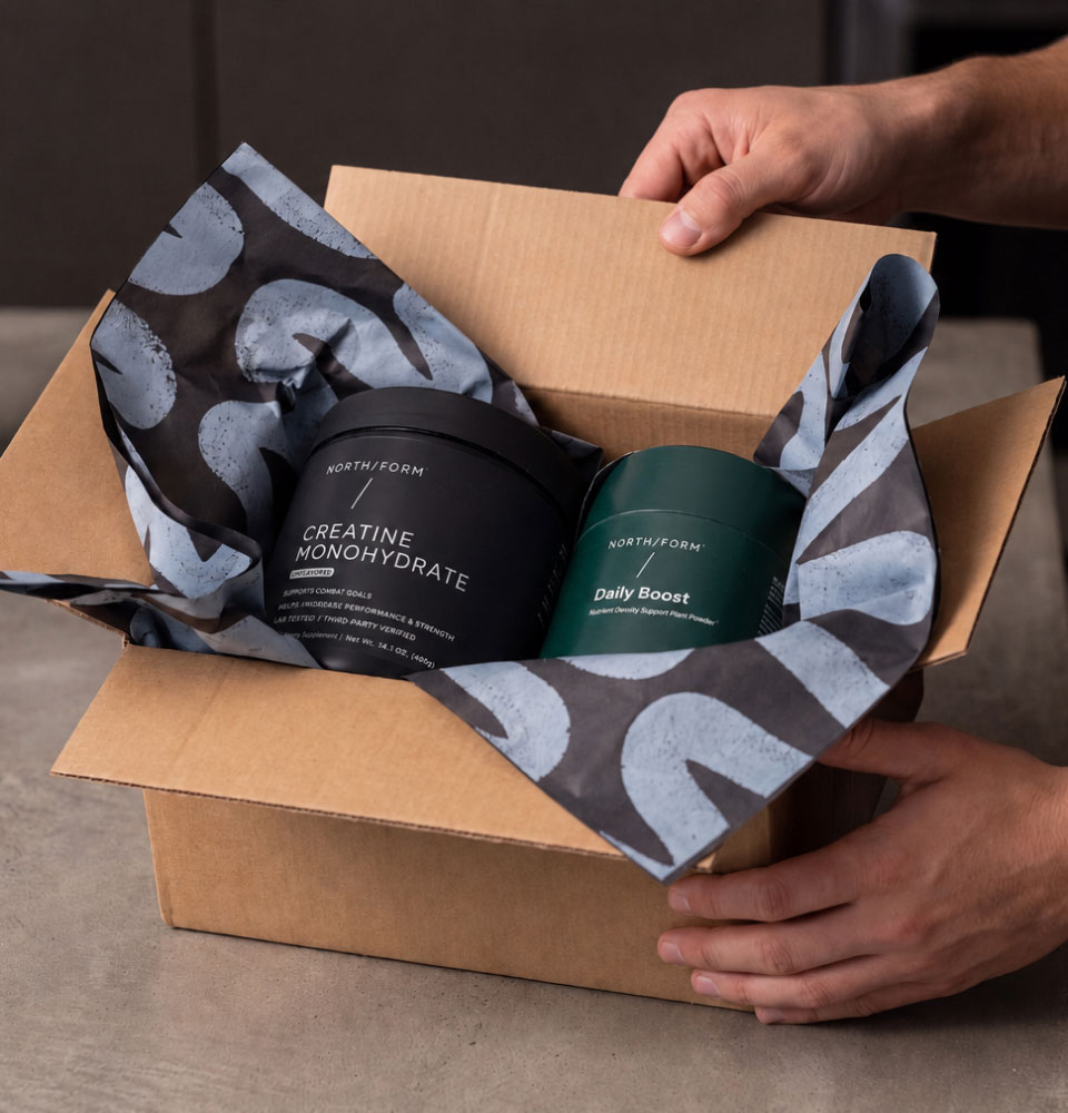 Two supplement containers, Creatine Monohydrate and Daily Boost, in a cardboard box with patterned packing paper.