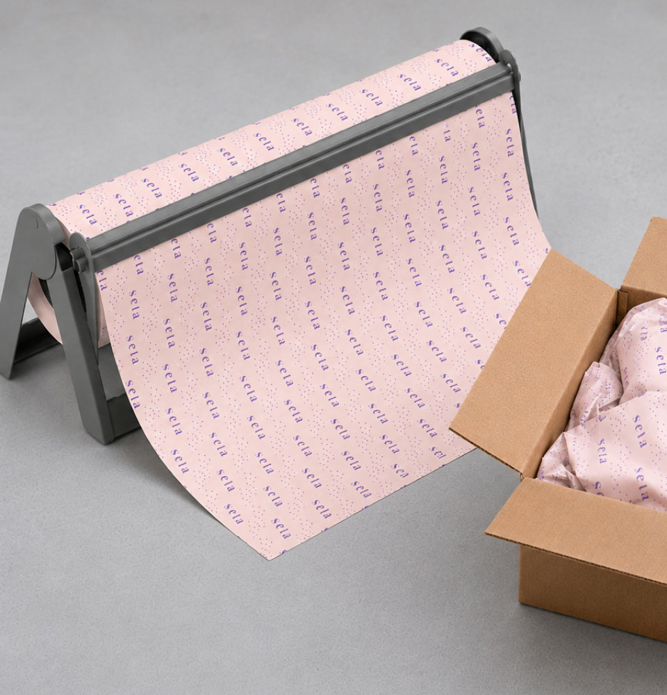A roll of pink packing paper with repeated purple 'seta' text on a gray dispenser next to a box with wrapped items.