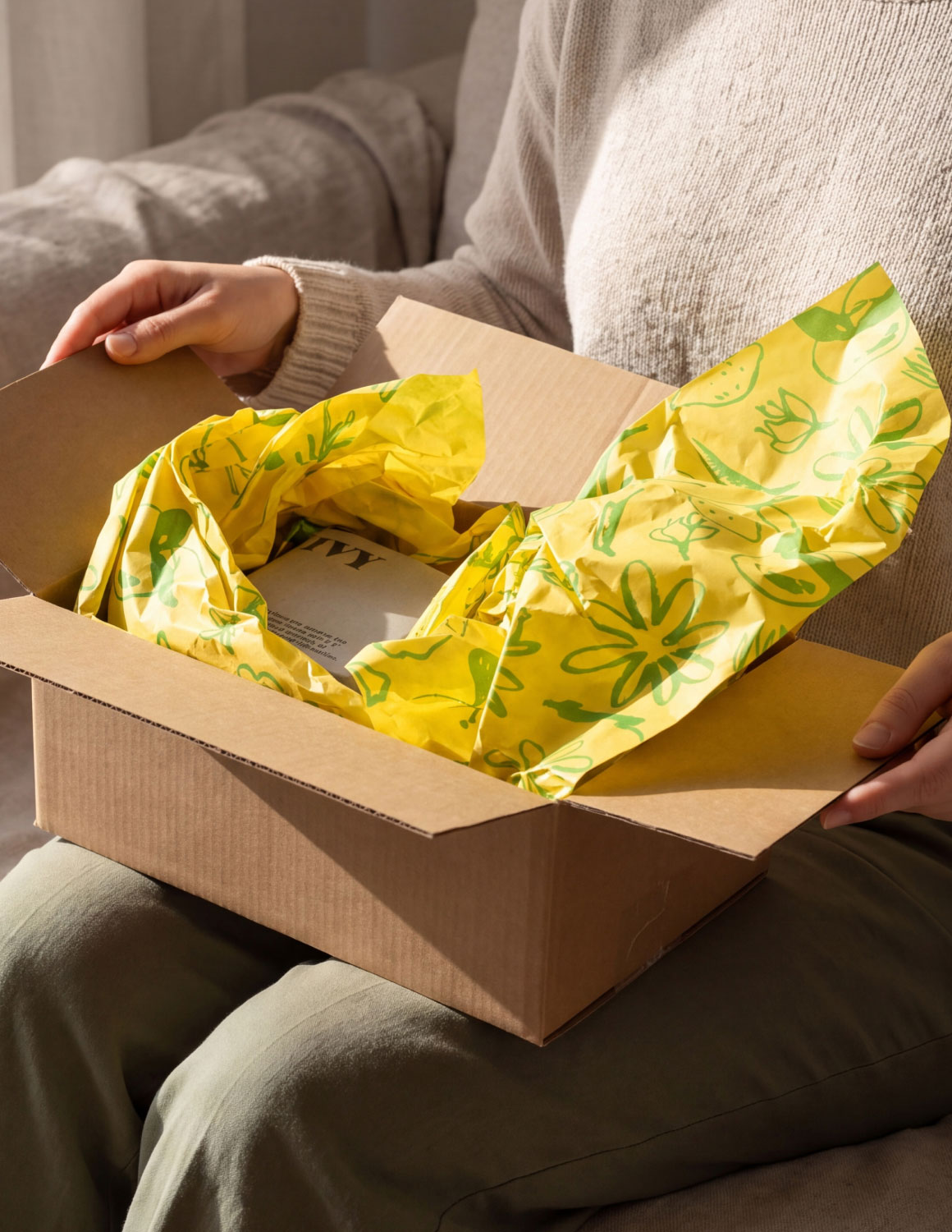 Person holding an open cardboard box with yellow floral packing paper inside.