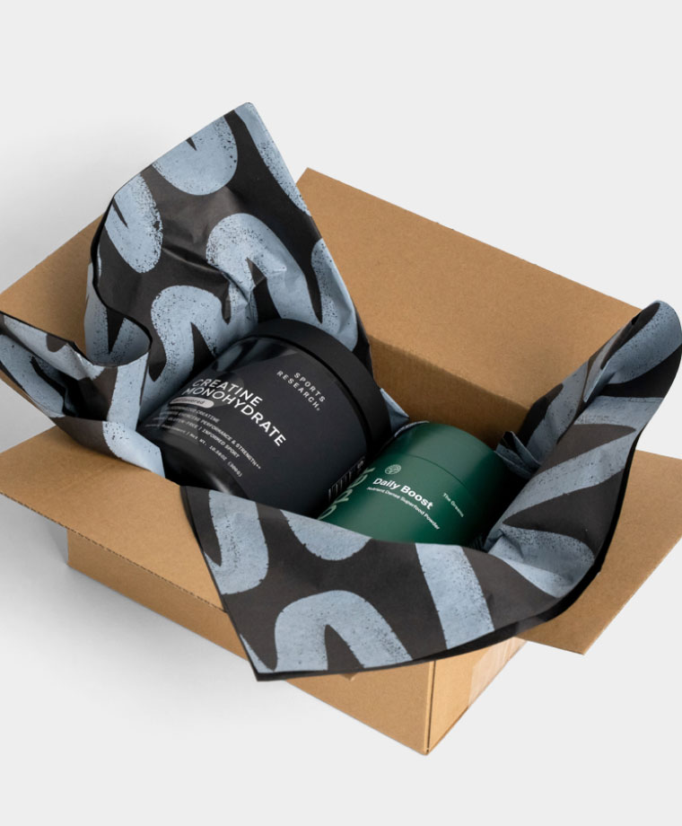 Two supplement containers, Creatine Monohydrate and Daily Boost, nestled in a cardboard box with patterned packing paper.