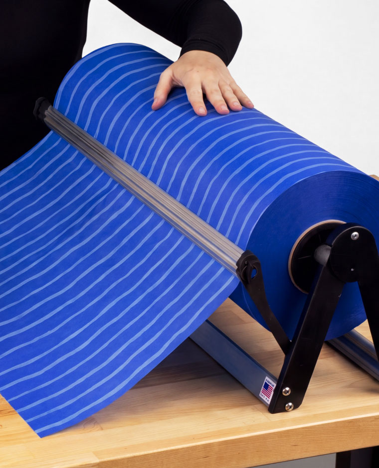 Hand pulling blue striped material from a roll on a black dispenser mounted on a wooden table.