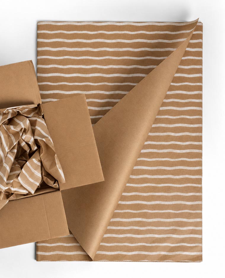 A piece of brown kraft paper with white horizontal stripes partially folded, next to an open brown cardboard box containing crumpled striped kraft paper.