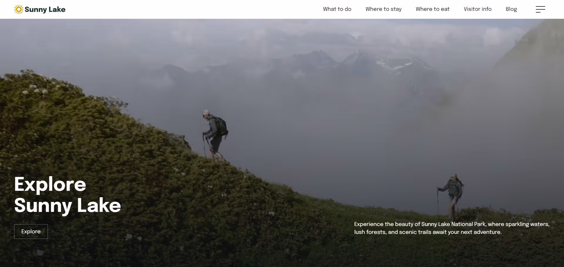 Two hikers with backpacks trekking on a green mountain slope under a cloudy sky with distant mountain peaks.