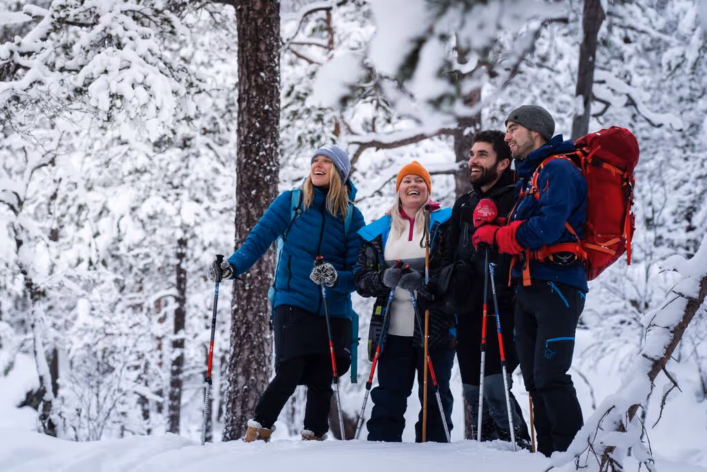 A cheerful group of snowshoers dressed in winter gear, pausing for a moment of laughter amidst a snowy forest.
