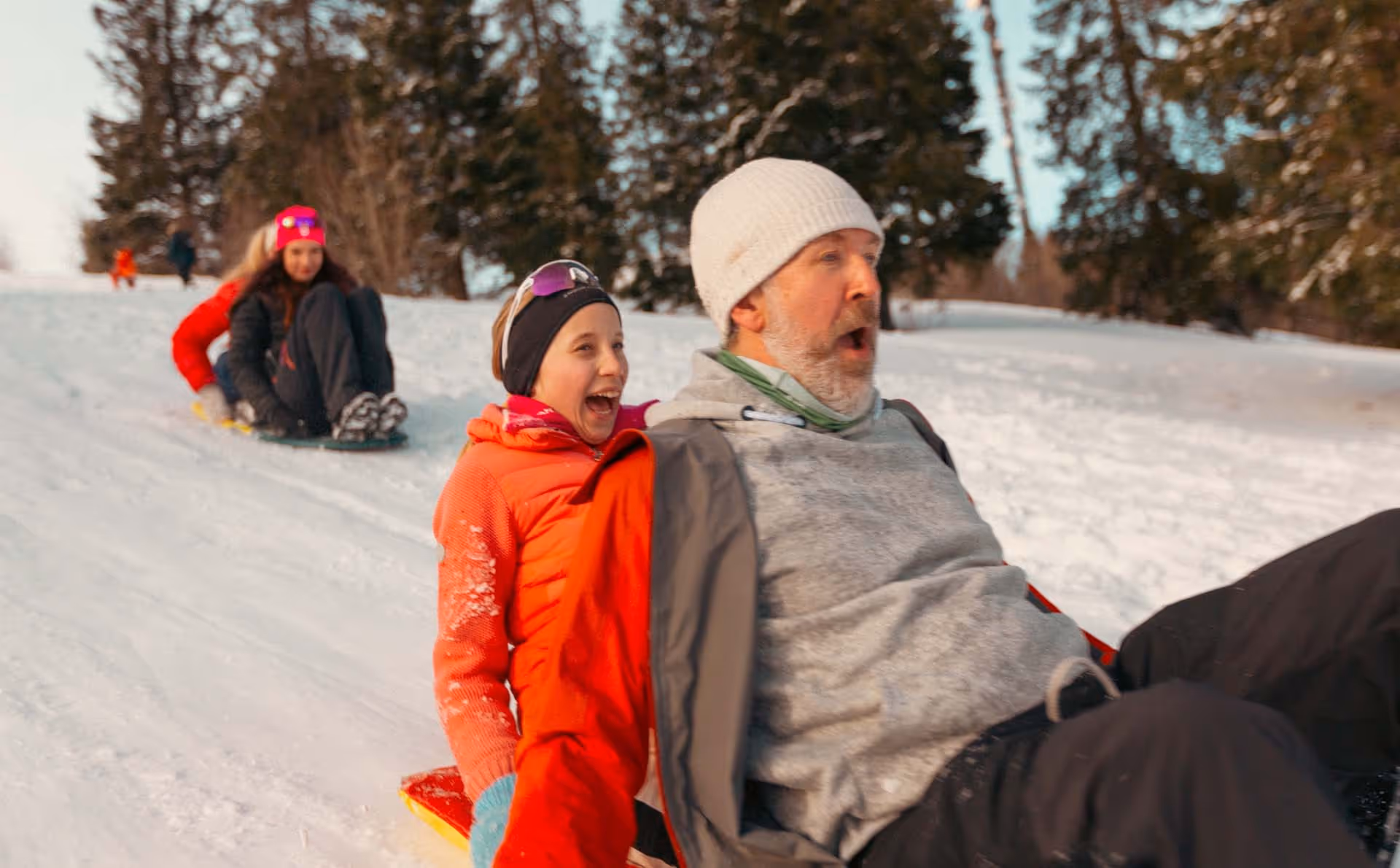 A joyful moment of sledding, as a man and child laugh and glide down a snowy slope with excitement.