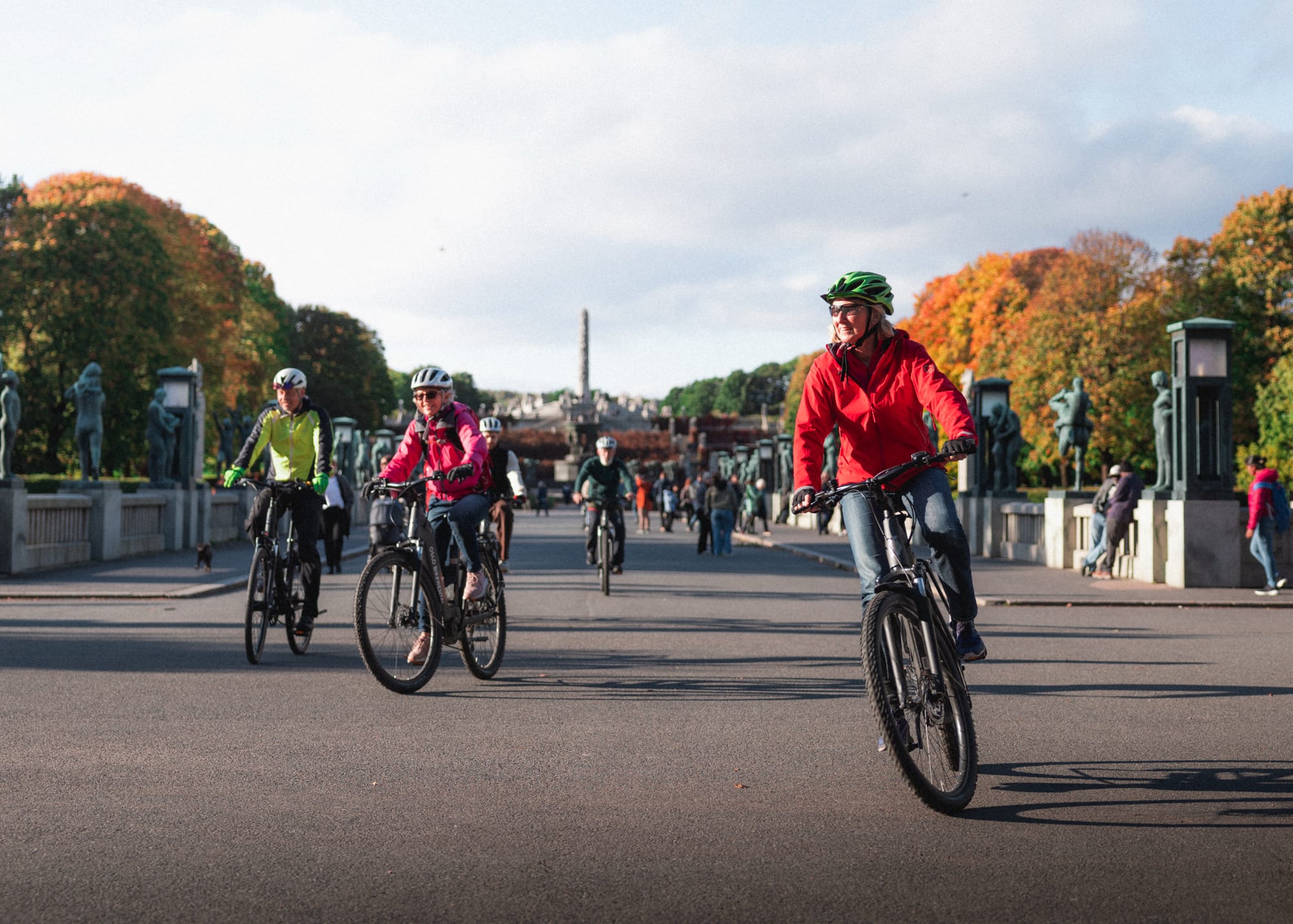Two cyclists ride along a tramline near the National Museum in Oslo. The modern glass building and surrounding urban architecture reflect the vibrant city atmosphere on a sunny day.