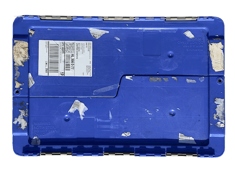 Blue plastic crate lid with worn and torn shipping labels and barcode stickers.