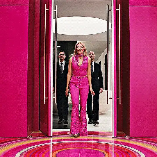 GIF image of Barbie walking through two opened doors with two men in suits trailing behind her