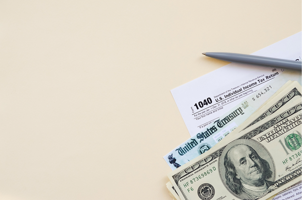 U.S. 1040 individual income tax return form with hundred dollar bills and a Treasury check on a beige background