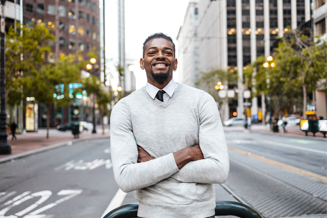 Smiling business professional with arms crossed standing on a San Francisco downtown street with office buildings and street lights in the background