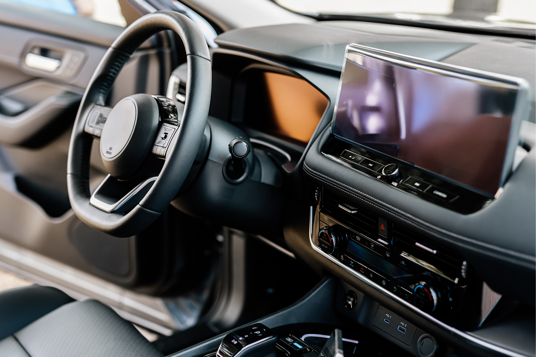 Modern car interior showing a black leather steering wheel, digital touchscreen display, and center console controls