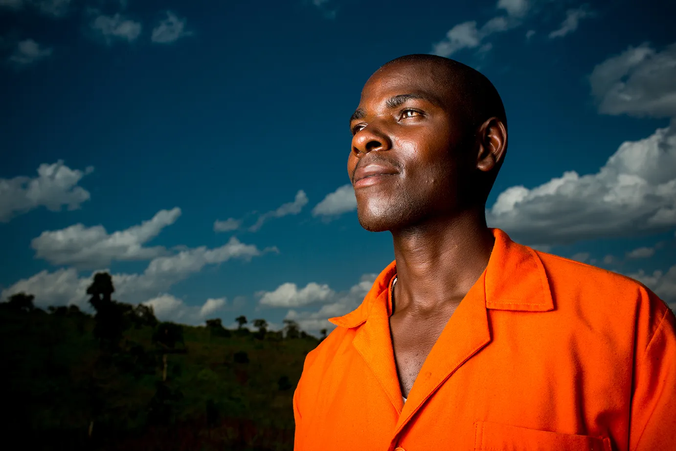 Man looking to the left into the distance against a blue sky with white clouds. 