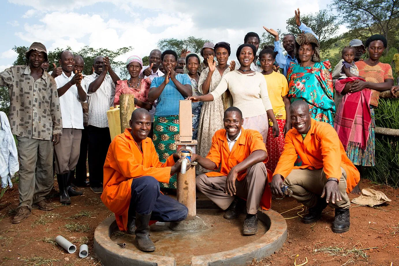 Three well mechanics squatting in front of well pump. Group of people smiling and celebrating while standing behind them. 