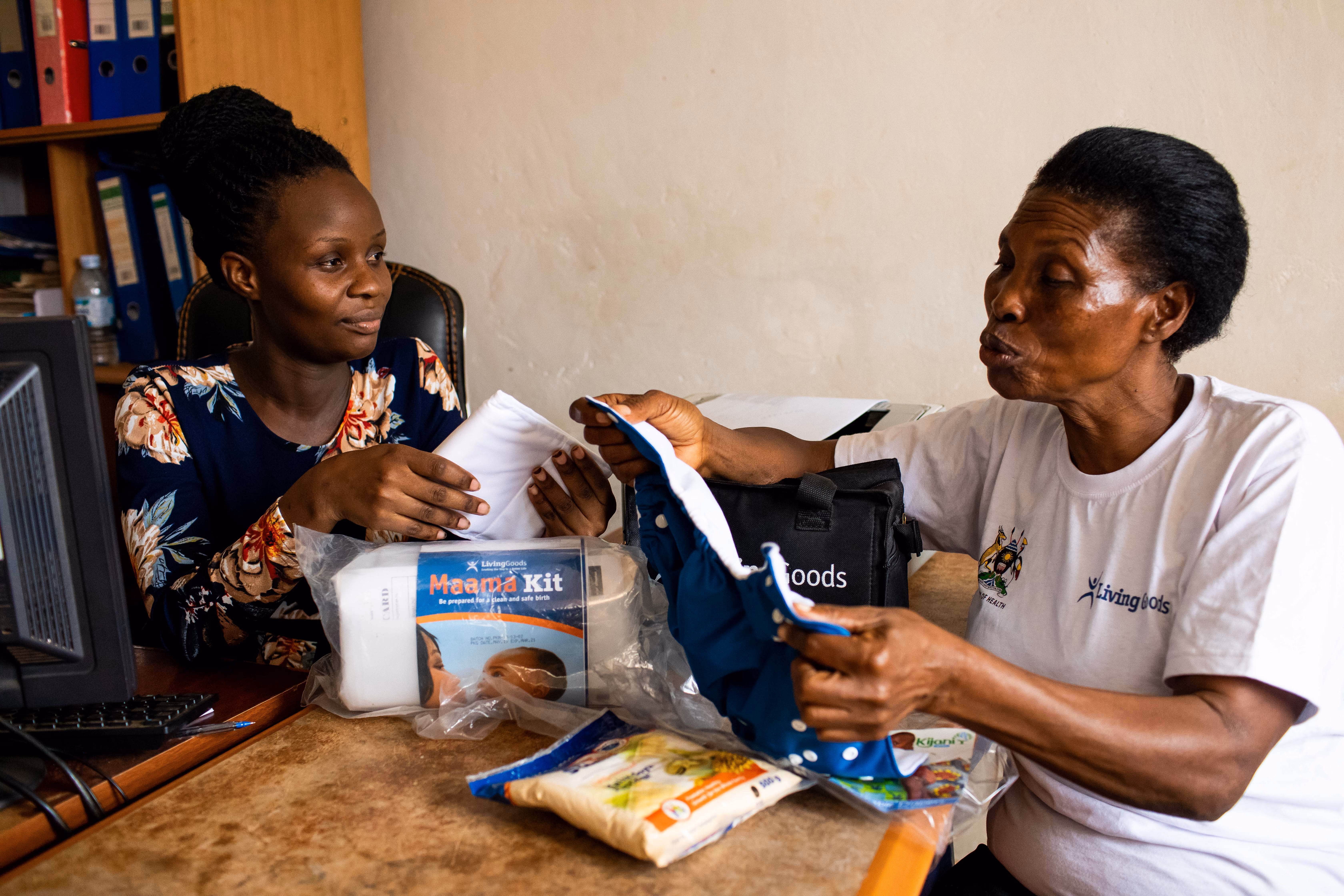 Community Health Worker counsels pregnant woman at a desk with various health products on display, including a Mama Kit. 