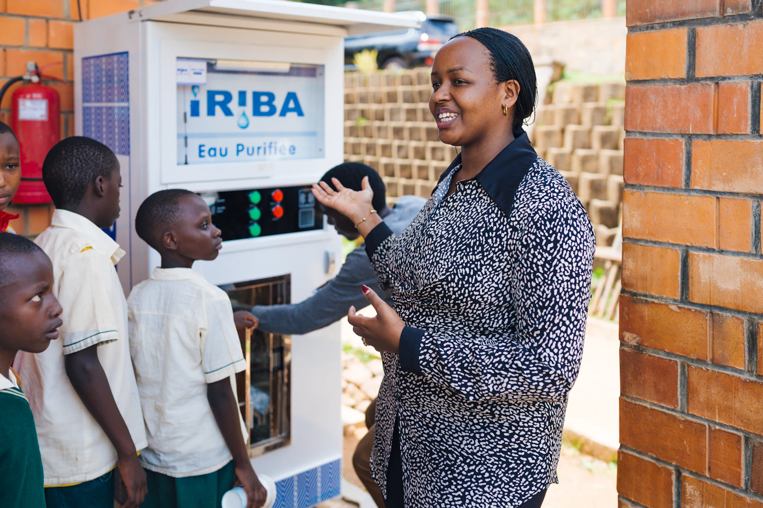 Yvette, the founder of Iriba Water Group in Kigali, stands next to a water ATM in a school in Rwanda.