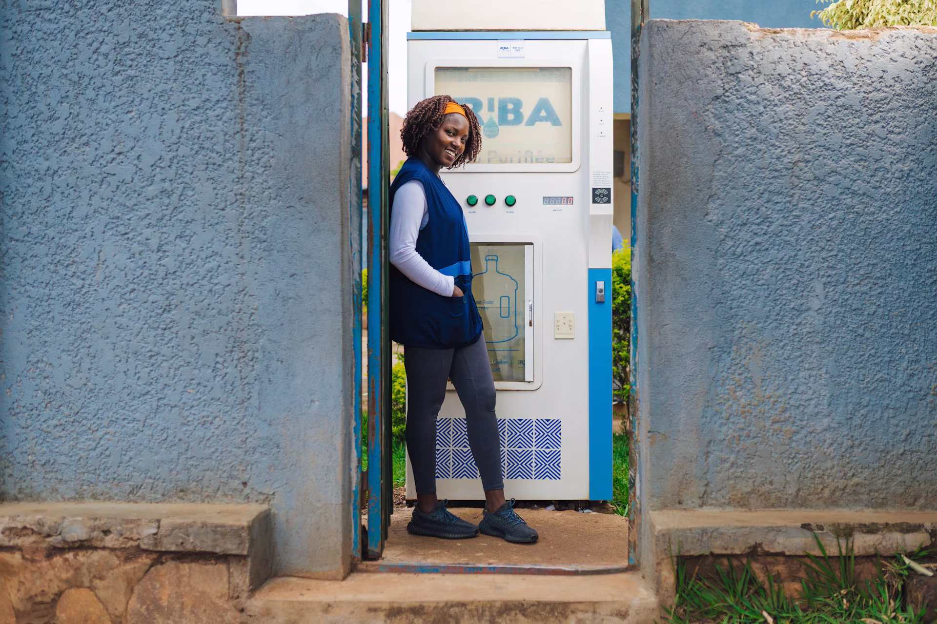 A woman water kiosk operator, smiling in front of her business in Rwanda.. 