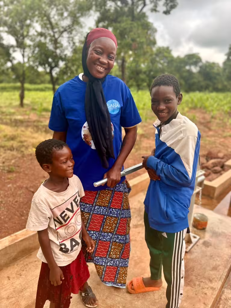 A mom and water well caretaker stands with her two kids at the well she maintains daily in Ghana.