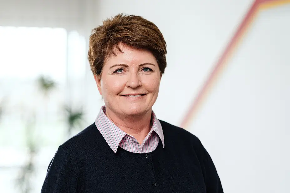 Porträt von Pamela Ritter mit kurzen braunen Haaren, schwarzem Oberteil über einem gestreiften Hemd, vor unscharfem Hintergrund.