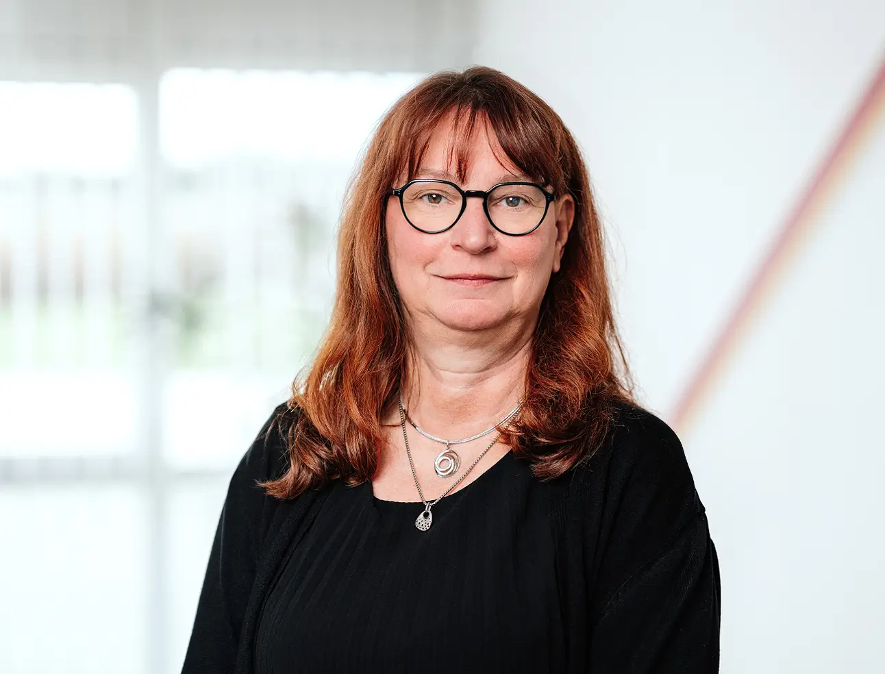 Frau mit schulterlangen braunen Haaren trägt schwarzen Pullover und zwei silberne Ketten vor unscharfem hellen Hintergrund.