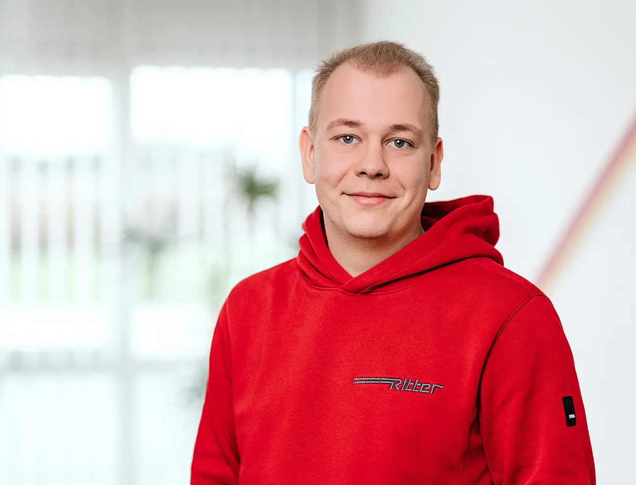 Person mit rotem Kapuzenpullover mit Schriftzug 'Ritter' vor hellem Hintergrund.