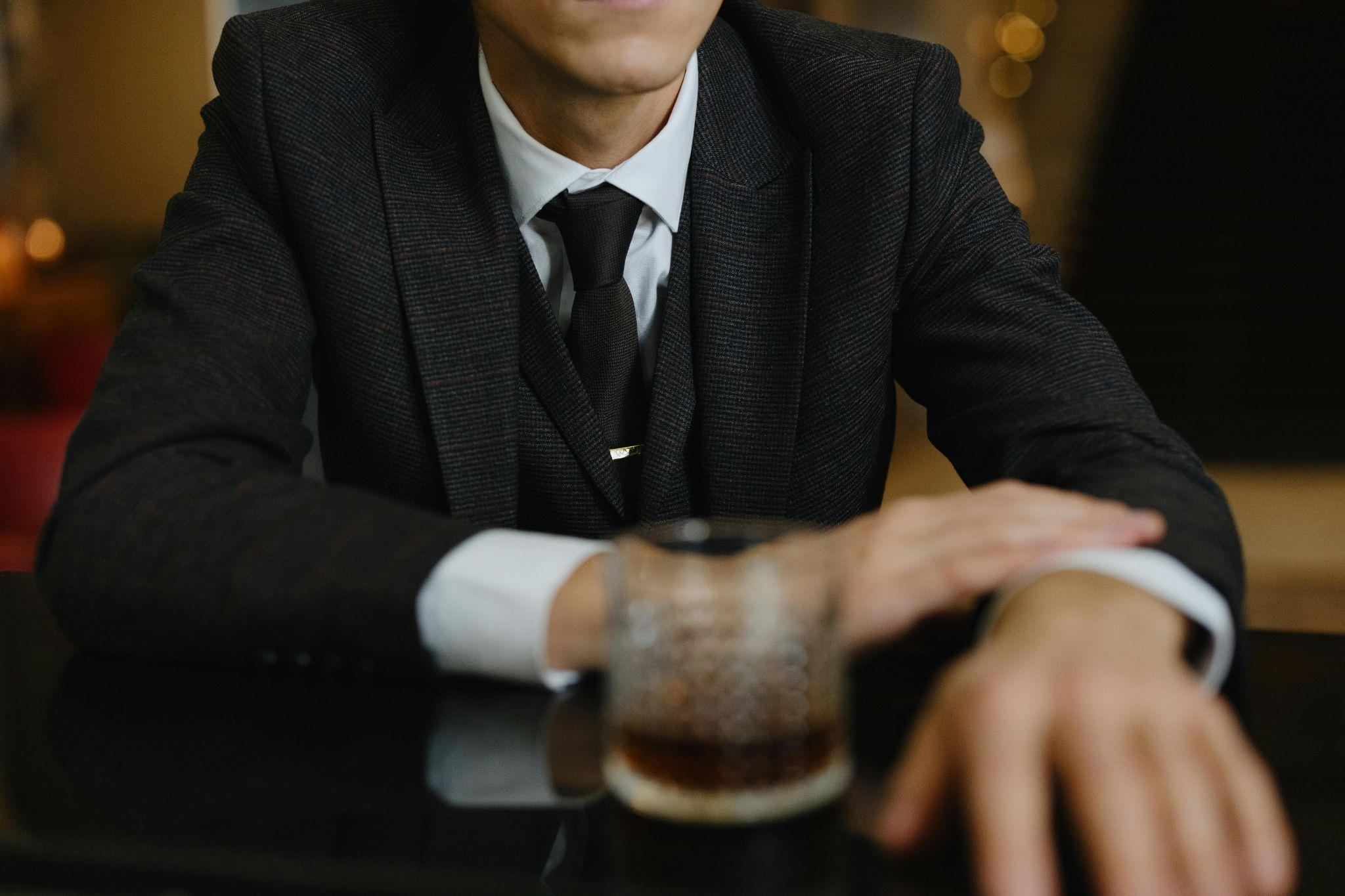 A man in a suit, sitting at a table with a drink.