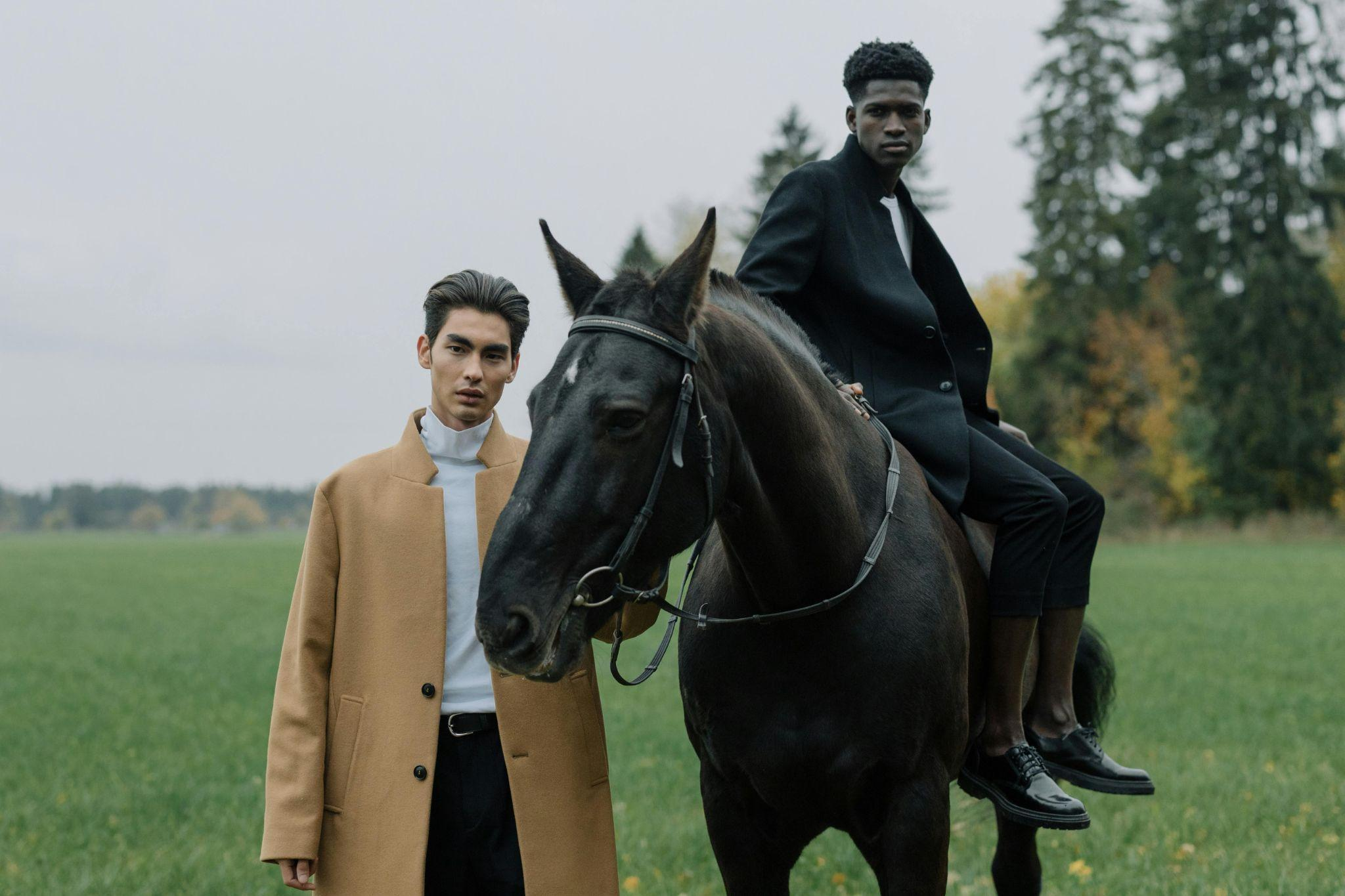 Two men standing with a horse in a field, both in coats.