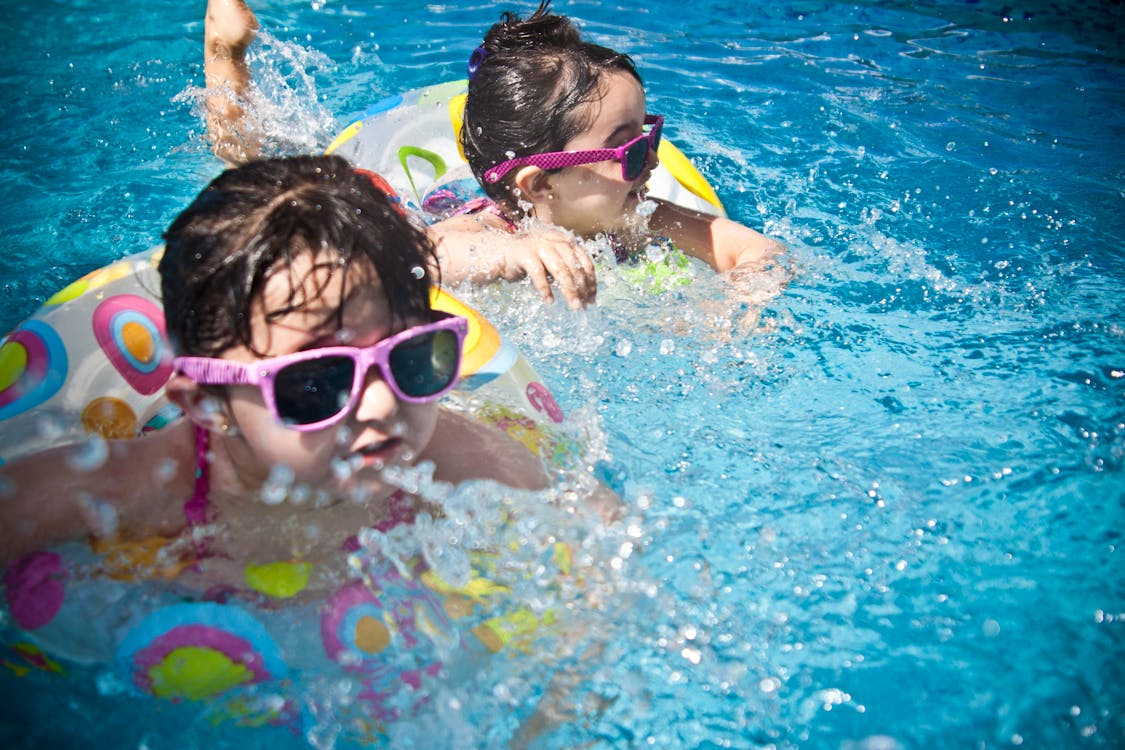 Two little girls are swimming in a pool wearing safety tubes