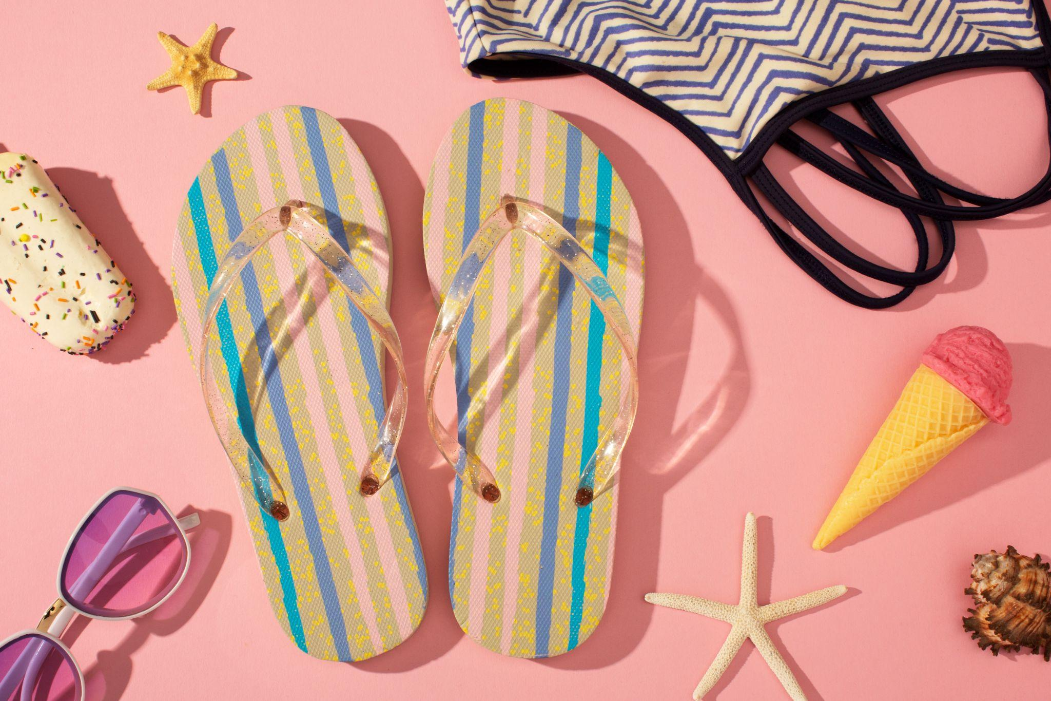 Flat lay of striped flip-flops, ice cream, and swimwear on a pink background
