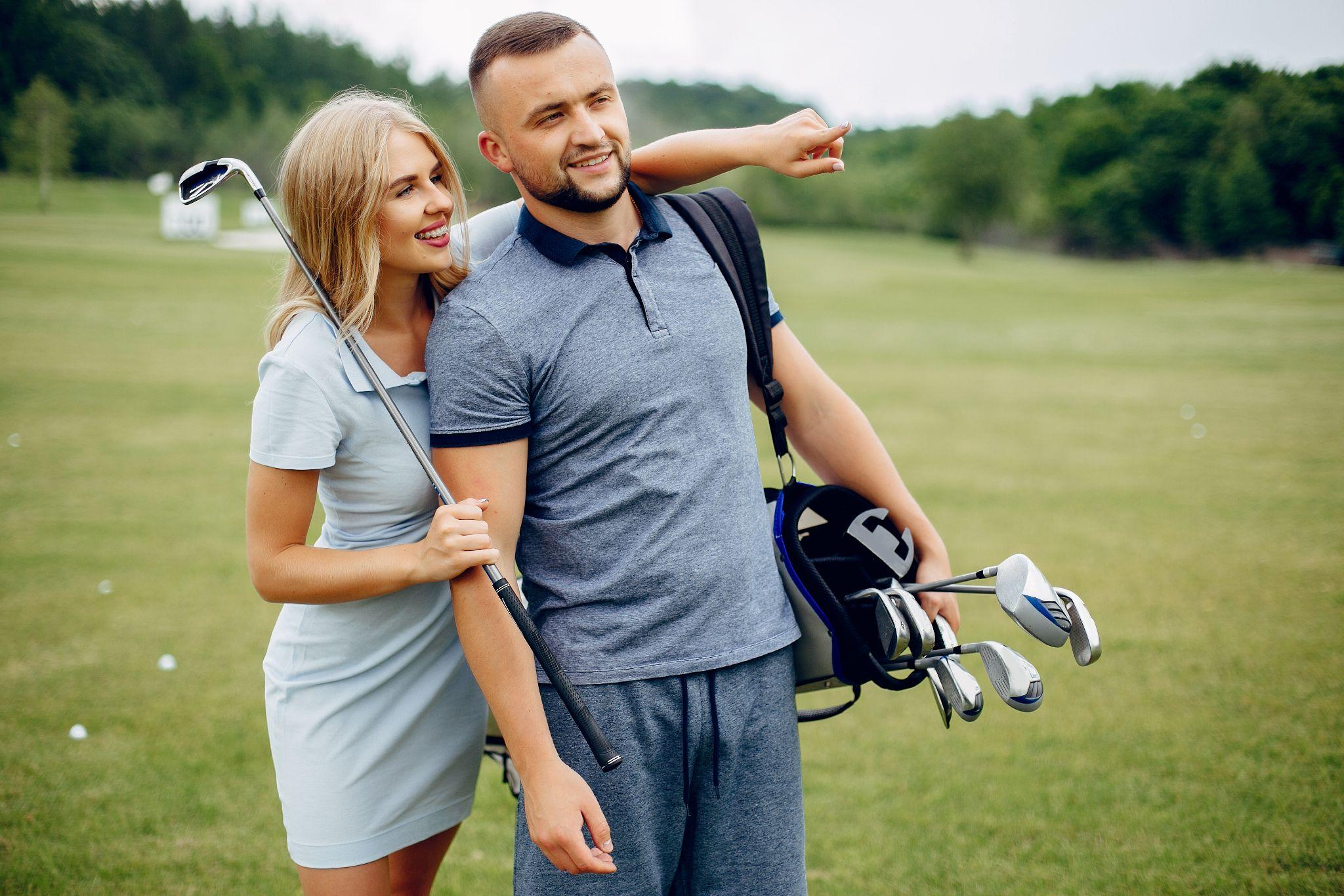Man carrying a golf bag and woman walking beside him on a green golf course.
