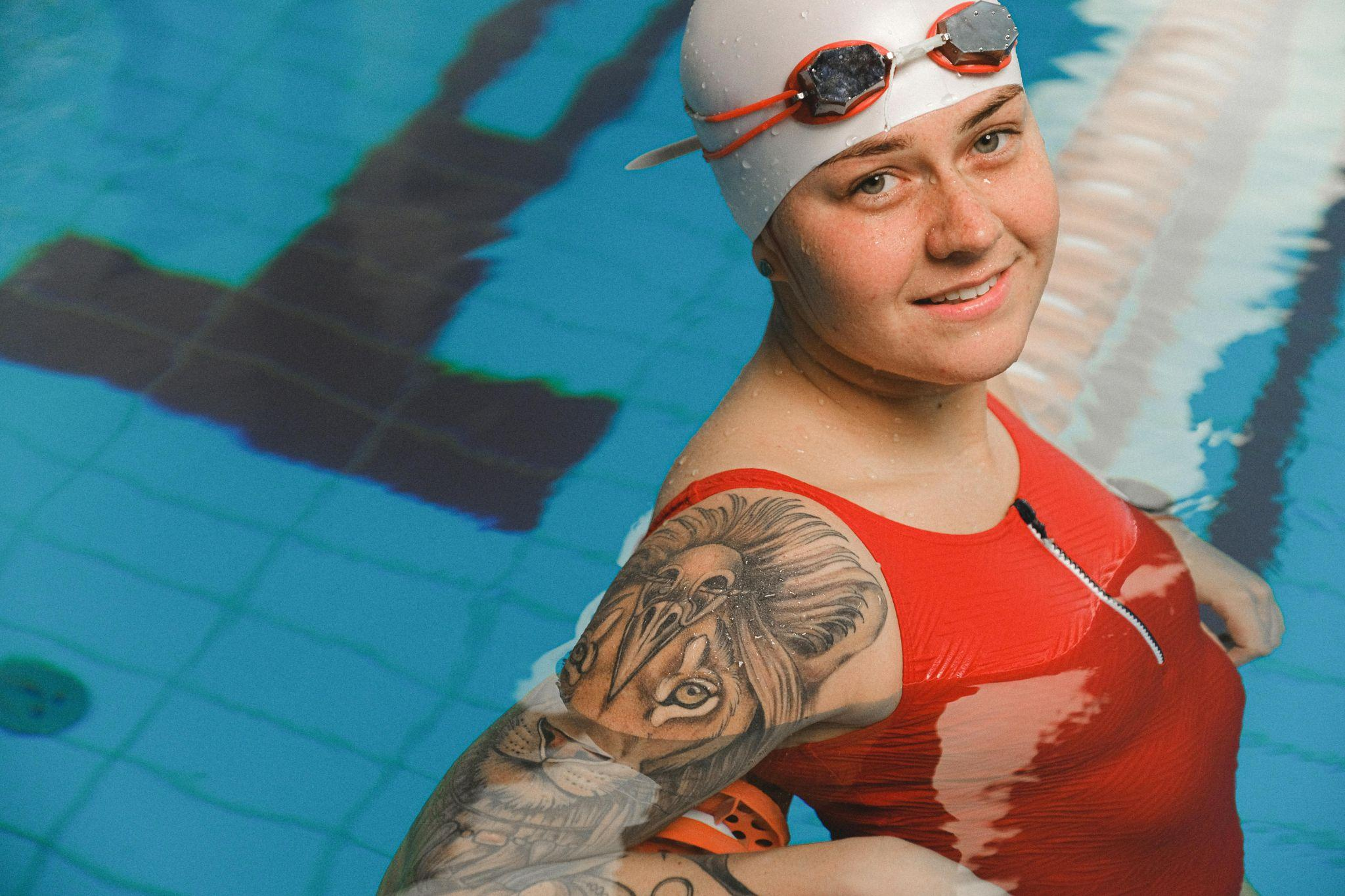 Smiling swimmer wearing a red zip-front swimsuit and swim cap