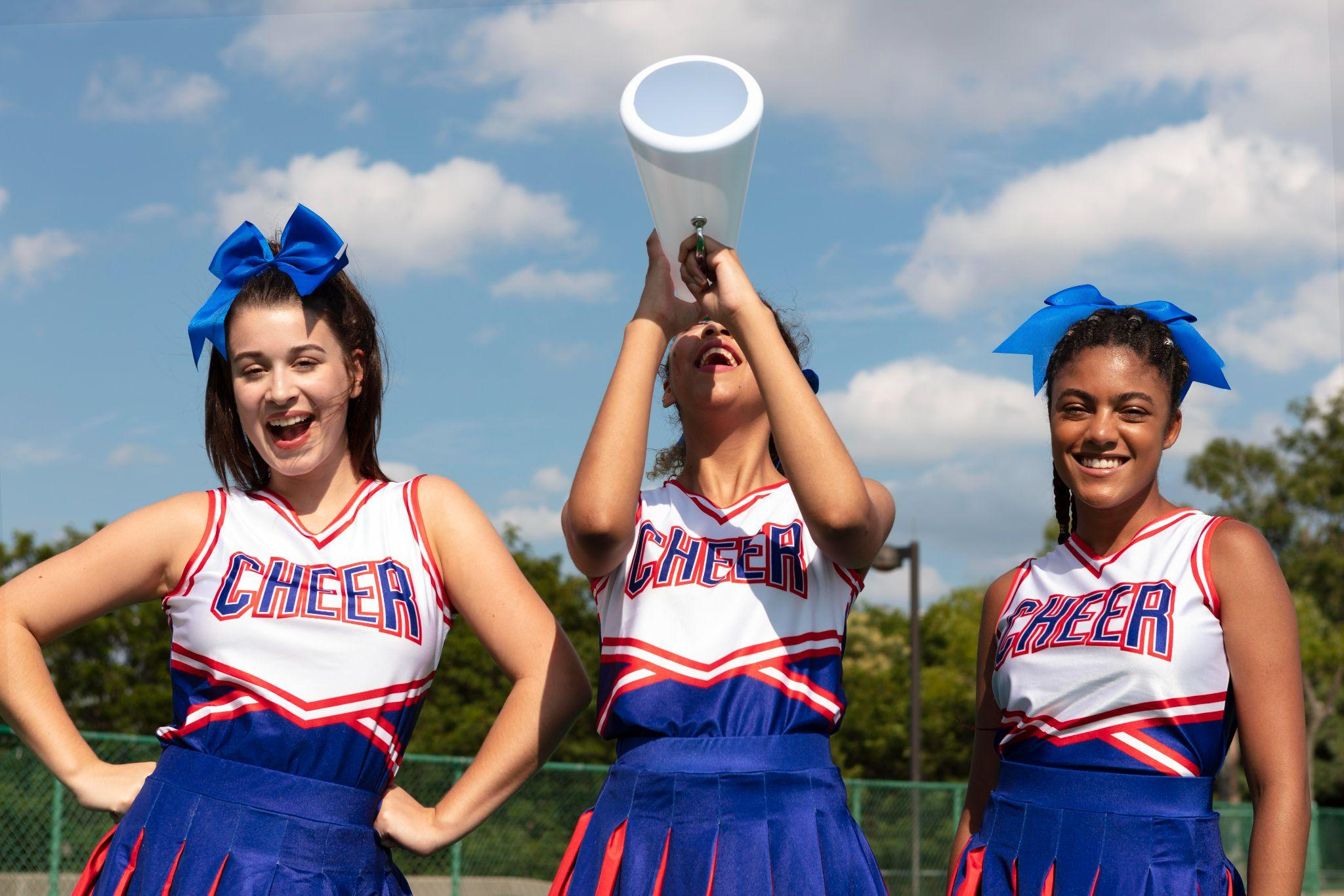 Three cheerleaders in matching uniforms, holding a megaphone.