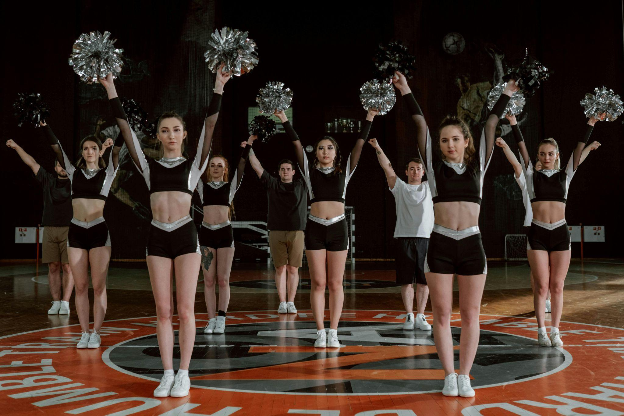 Cheerleading team in black uniforms performing a routine on a basketball court.