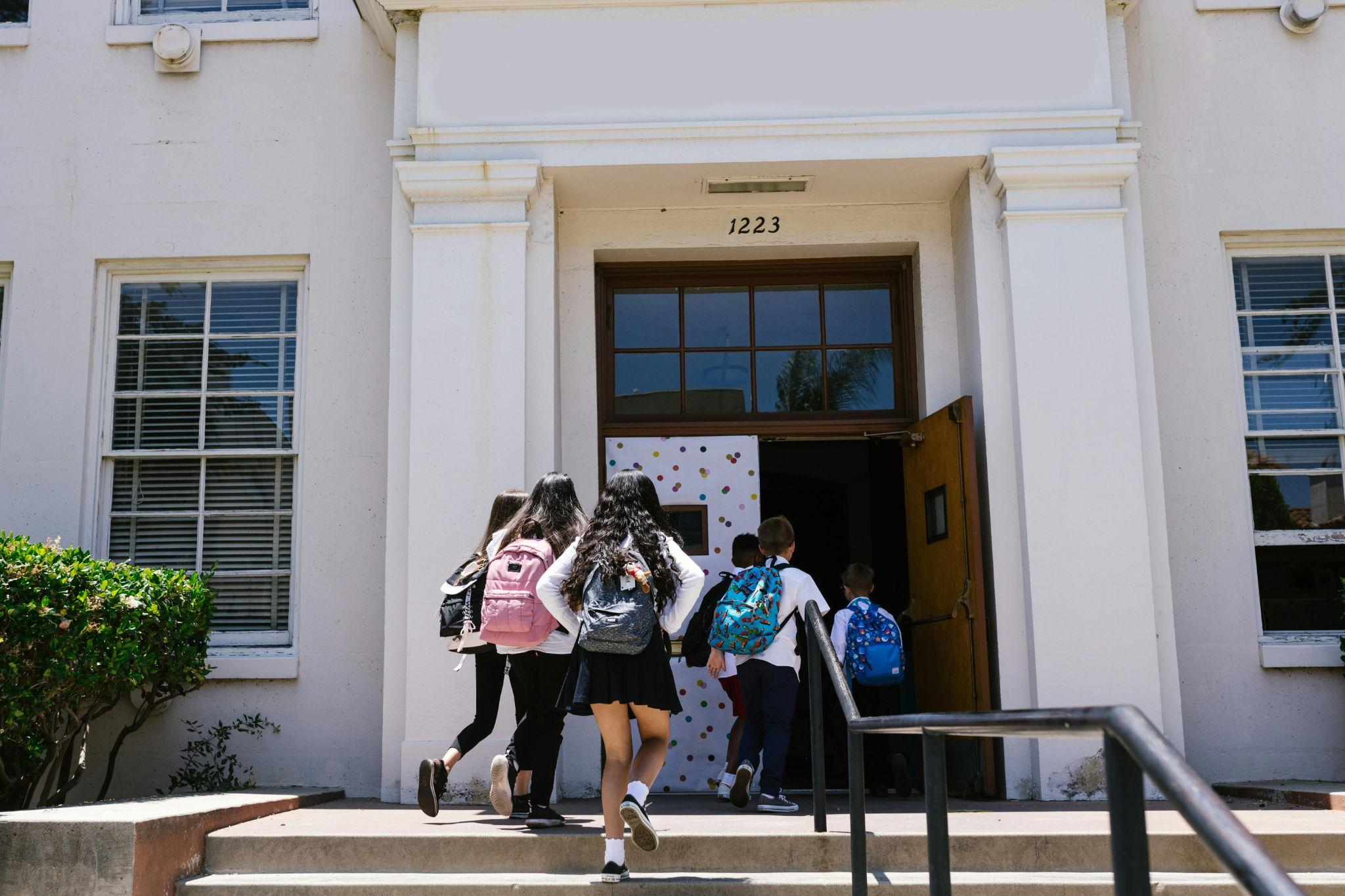 Group of students walking up steps into a school building with backpacks.