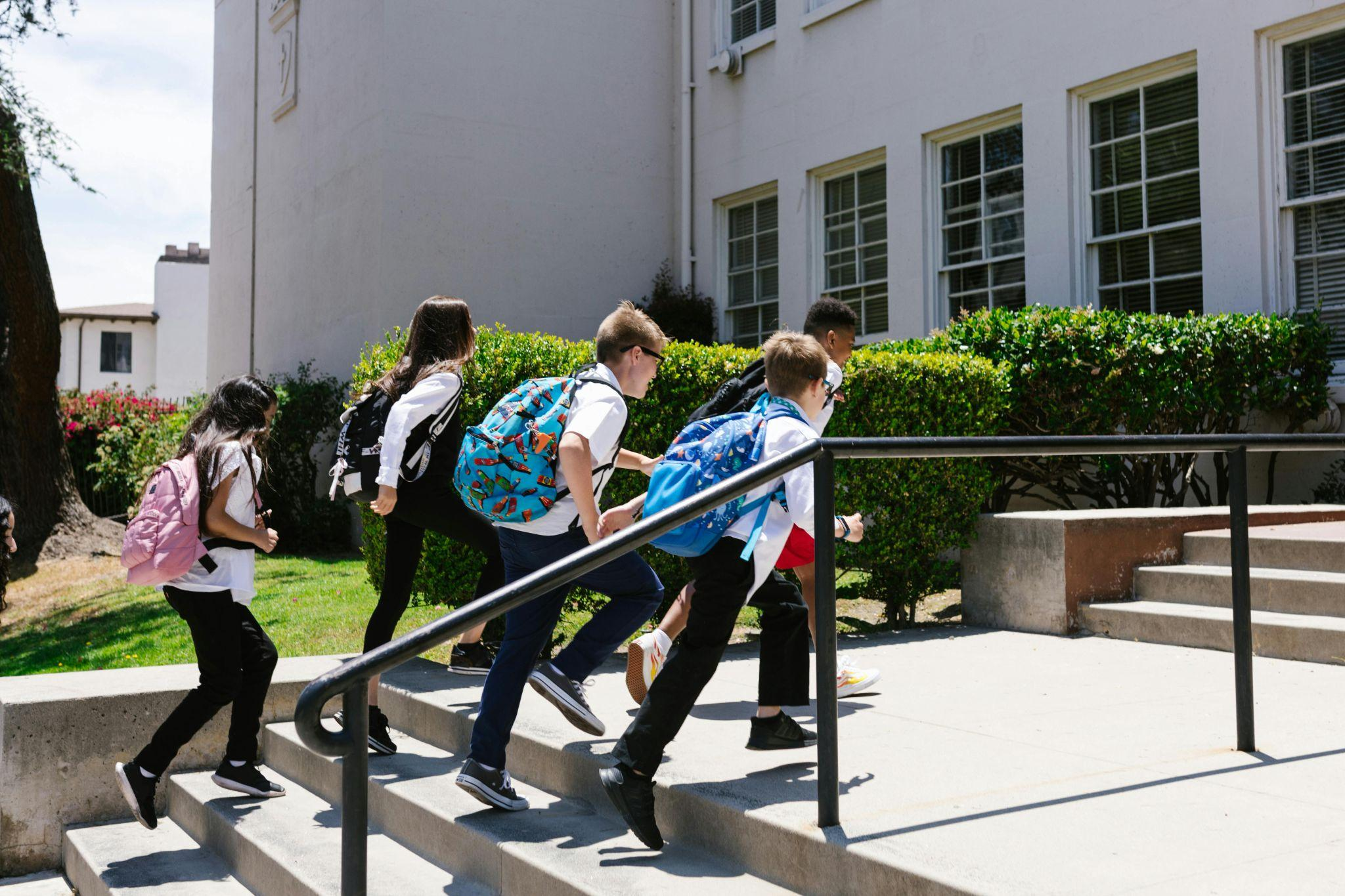 Students wearing backpacks and uniforms walking near a school building.