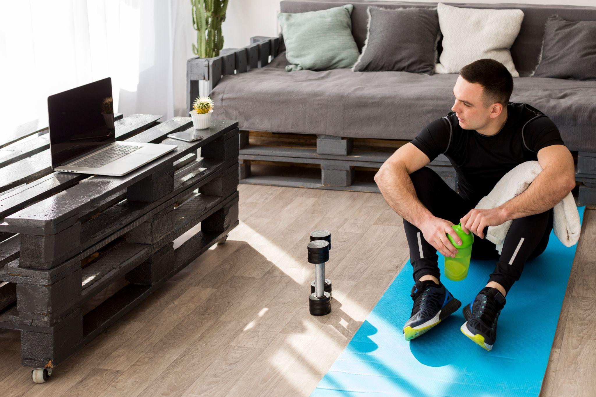 Man in compression sportswear sitting on a yoga mat indoors, preparing for a workout.