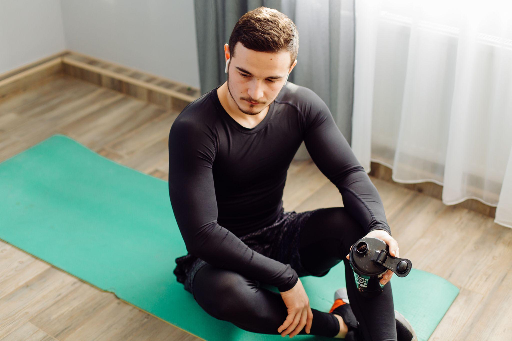 Man wearing a black compression top seated on a green exercise mat