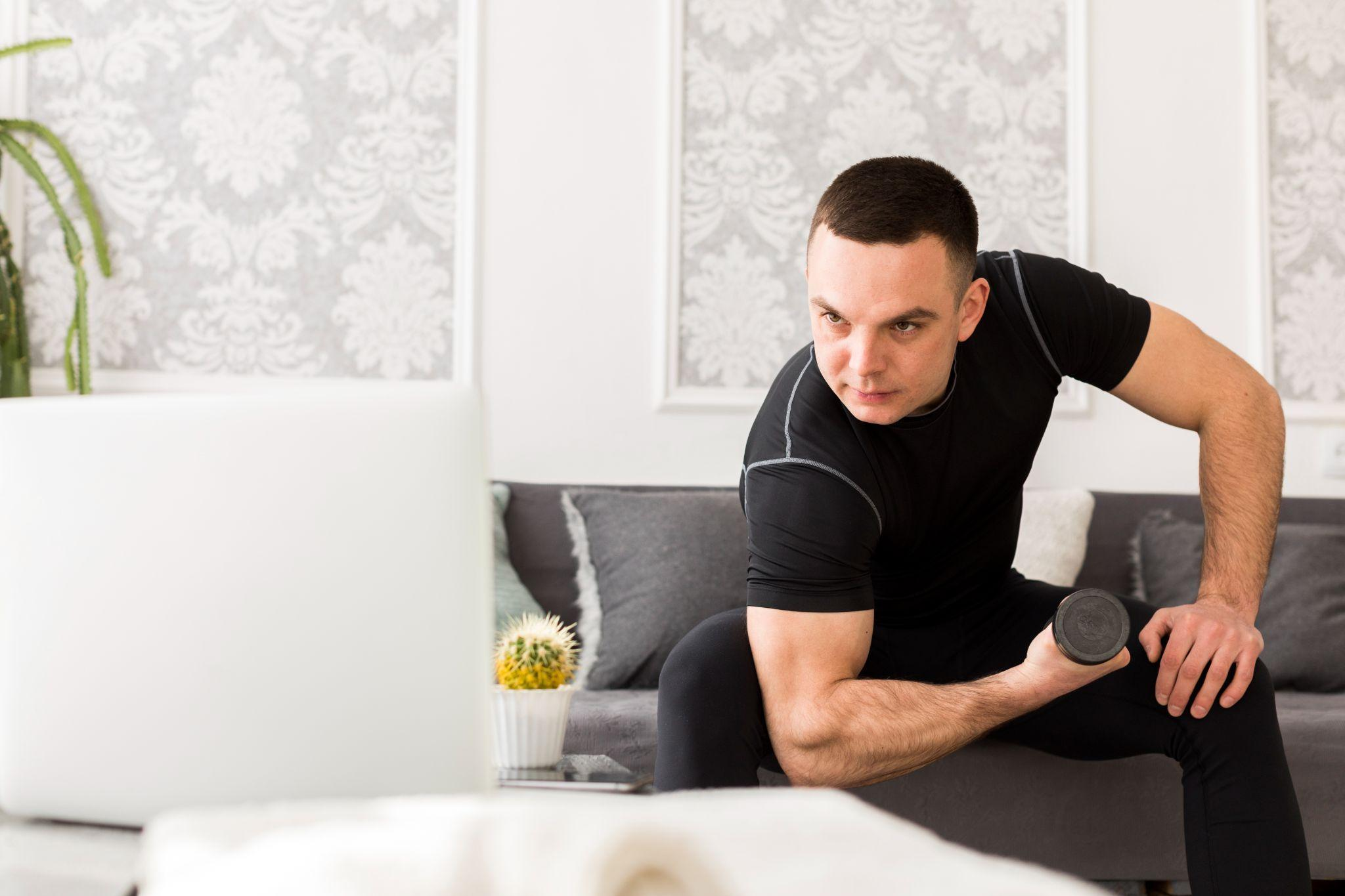 Man wearing a black compression shirt performing a dumbbell row exercise at home.