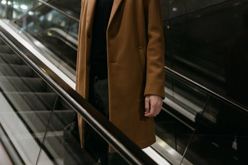 A person in a brown coat standing on an escalator