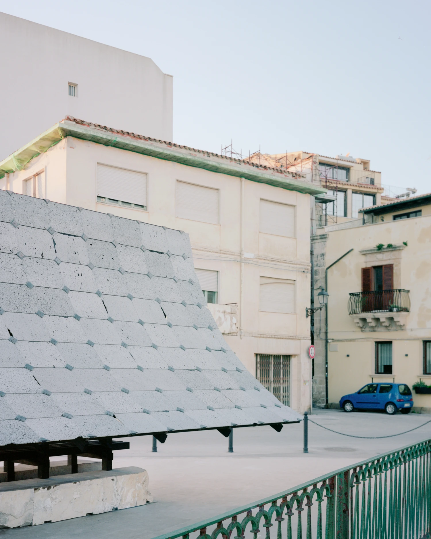 Pantalica Speculations by Leopold Banchini, An asymptotic timber and stone pavilion on a seaside promenade overlooking the Mediterranean, dark wood frame supporting stone-tile roof on massive limestone blocks