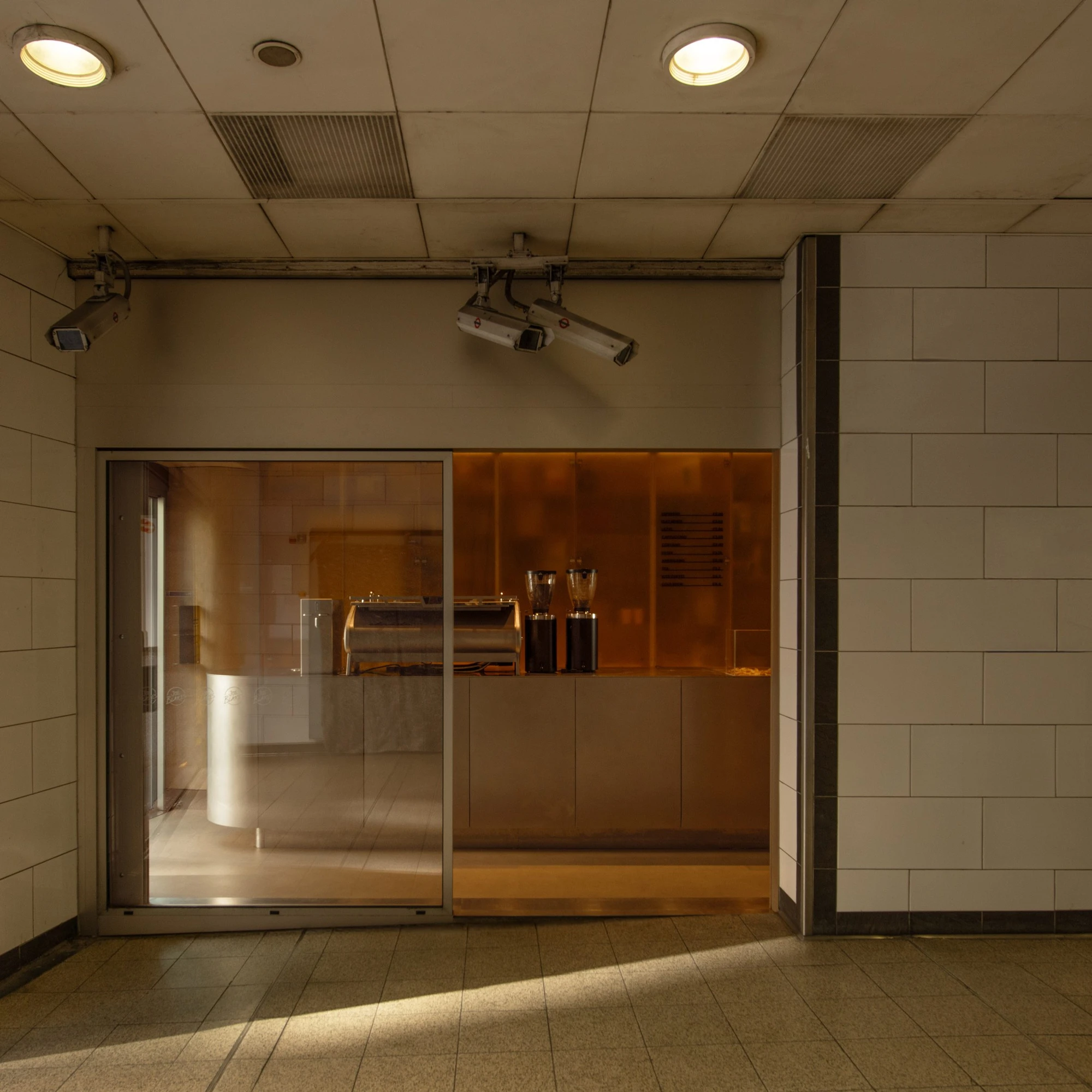 Joe Blake's Holborn coffee shop by EBBA in London tube station, minimalist interior with rounded stainless steel counter and milky translucent storage wall, sand-coloured plaster ceiling