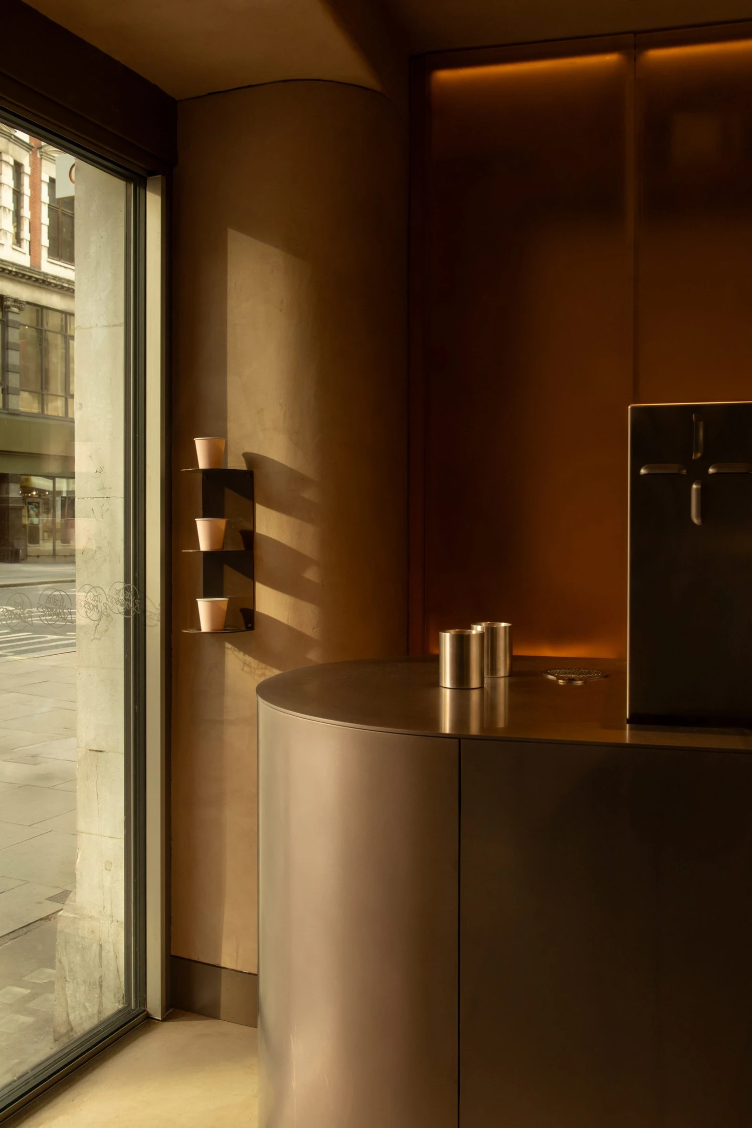 Joe Blake's Holborn coffee shop by EBBA in London tube station, minimalist interior with rounded stainless steel counter and milky translucent storage wall, sand-coloured plaster ceiling