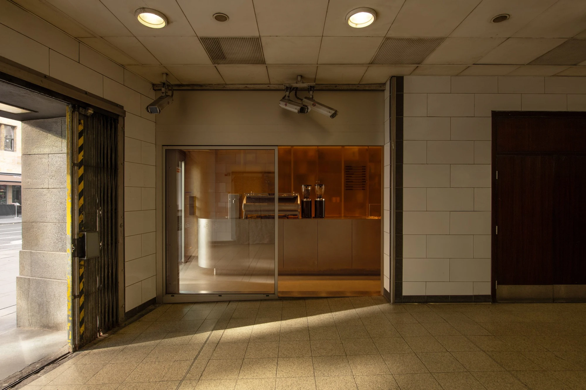 Joe Blake's Holborn coffee shop by EBBA in London tube station, minimalist interior with rounded stainless steel counter and milky translucent storage wall, sand-coloured plaster ceiling